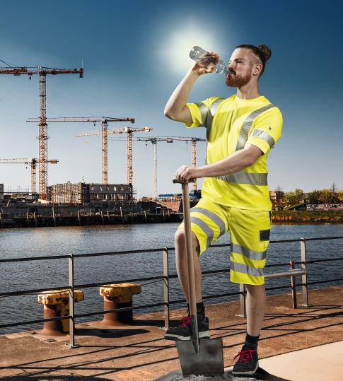 Un employé des chemins de fer porte des vêtements de travail avec protection contre les UV à côté d'un train qui dégage de la vapeur.